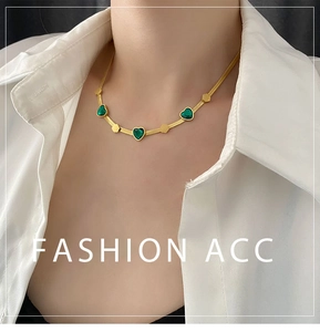 Detail of gold snake chain necklace featuring three emerald heart pendants on a model