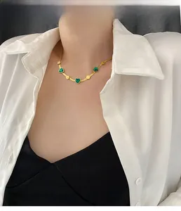 Detail of model wearing a gold necklace featuring three heart-shaped emerald green stones