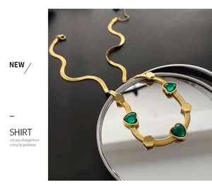 Detail of gold snake chain necklace with emerald green heart-shaped gems on mirror