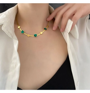 Close-up of gold snake chain necklace featuring green malachite heart charms on model