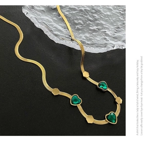 Close-up of golden flat snake chain necklace with emerald green heart-shaped gemstones