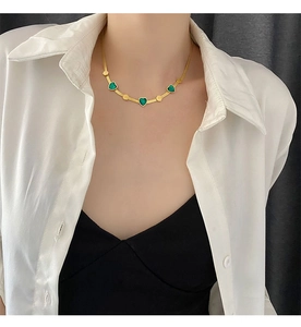 Detail of a golden flat snake chain necklace with emerald green heart-shaped pendants