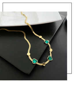 Detail of emerald green heart gems on a golden herringbone chain necklace for women