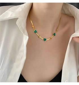 Detailed shot of emerald heart necklace on gold snake chain worn by a female model