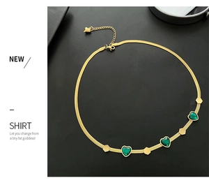 Detail of gold snake chain necklace with green heart gems and hexagonal metal accents