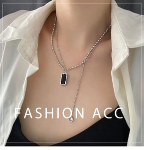 Detail of layered silver necklace with black pendant and tassel chain on model