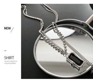 Macro shot of silver layered chain necklace featuring a rectangular black pendant on mirror
