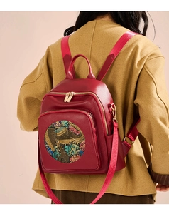 Detail of red pebbled leather backpack with elephant floral embroidery on yellow coat