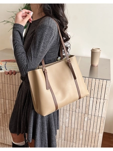 Detail of a large beige leather tote bag with slim brown shoulder straps for daily use