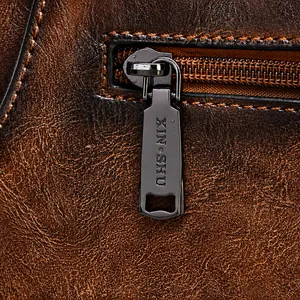 Close-up of vintage brown leather handbag featuring engraved metal zipper pulls and texture