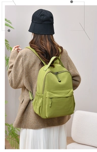 Detailed back view of a water-resistant green nylon backpack worn by a model in a room