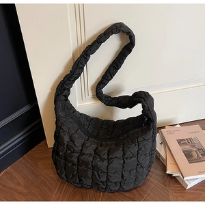 Détail de la texture d'un sac bulle noir matelassé en nylon brillant sur sol en bois