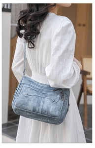 Blue-grey washed leather crossbody bag with multiple zippers and rivets shown on model