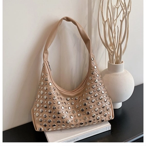 Detail view of khaki hobo bag with silver studs placed on white books in a minimalist setting