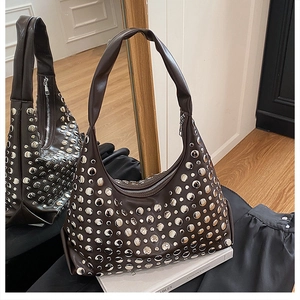 Detailed close-up of dark brown hobo bag with silver metallic studs on a white book