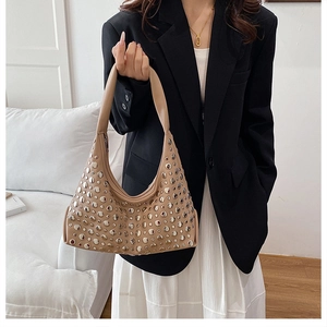 Close-up of beige underarm bucket bag with silver studs worn by model in black blazer