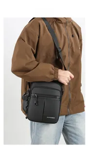Detail of a black multi-pocket oxford crossbody bag worn by a model in a casual business style