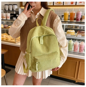 Detail of light green corduroy backpack showing textured fabric and woven zipper pull