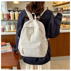 Detail of white corduroy backpack with dual zippers shown on model in cozy cafe setting
