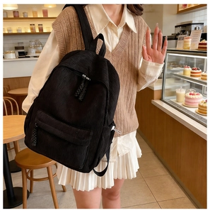 Detail of black corduroy backpack showing vertical ribbed texture and woven zipper pullers