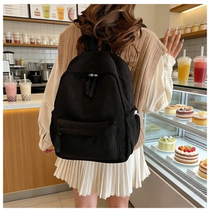 Close-up of black corduroy backpack with woven rope zipper detail in a cozy cafe