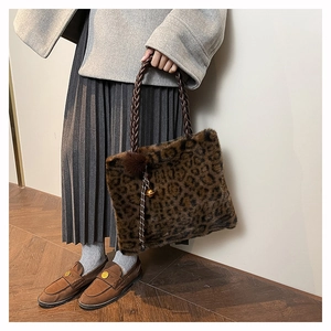 Detail of leopard print faux fur tote bag with woven handles and pompom charm on a model