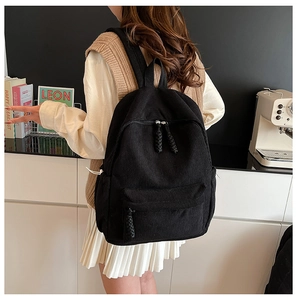 Detail of black corduroy backpack showing textured fabric and side storage pockets