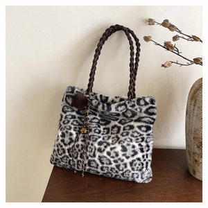 Detail of leopard print plush tote bag with brown woven handles and pom-pom charm decoration