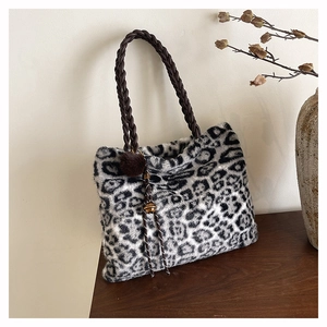 Close-up of leopard print plush tote with woven handles and a brown pompom charm