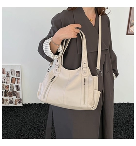 Detail of cream tote bag featuring textured leather, vertical zippers, and side pockets