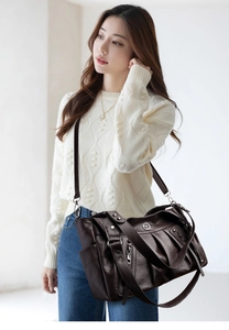 Detail of dark brown tote bag featuring pleated leather texture and decorative metal logo