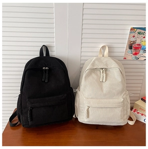 Detailed view of textured corduroy backpacks in black and beige on wooden table
