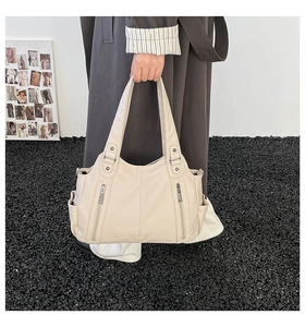 Detail of off-white tote bag showing side pockets and decorative zippers on soft PU leather