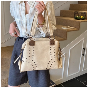 Detail of beige tote bag showing metal rivets and reinforced brown leather handle accents