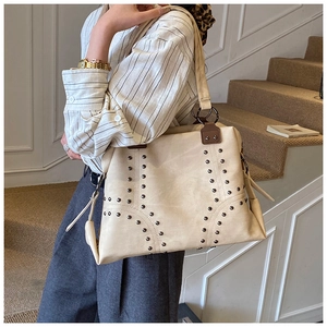 Detailed view of beige tote bag featuring metal rivets and wide shoulder strap