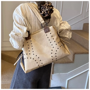 Close-up of beige tote bag with metallic rivet accents and premium brown leather straps