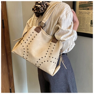 Detail of off-white leather tote bag featuring metallic rivets and stylish side tassels