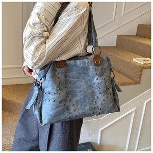 Close-up of blue tote bag with rivet X-pattern and leather handle on shoulder