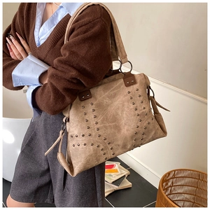 Vintage khaki tote bag with metal rivets shown on model in a cozy indoor setting