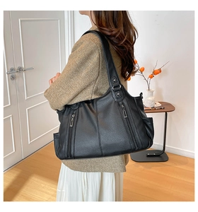 Detail of black pebbled leather tote bag with functional silver vertical zippers and wide strap