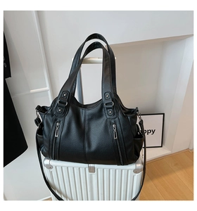 Detail of a black pebbled leather tote bag with functional zippers and silver hardware
