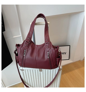 Detail of burgundy lychee leather tote bag placed on a white suitcase for travel