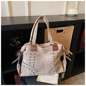 Detail of beige suede tote bag with metal studs and zipper closure on a wooden shelf