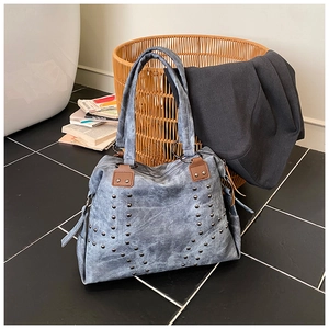 Detail of blue denim tote bag featuring silver rivet V-shape pattern and brown leather handles