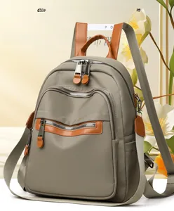 Detailed view of grey-green nylon backpack featuring brown leather accents and multi-layer zippers