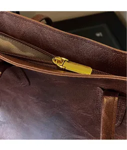 Macro view of the shiny gold zipper and premium brown oiled leather texture of the tote bag