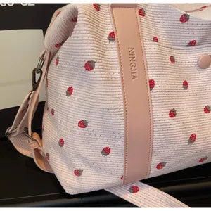 Close-up of strawberry embroidery on pink corduroy fabric and leather strap details