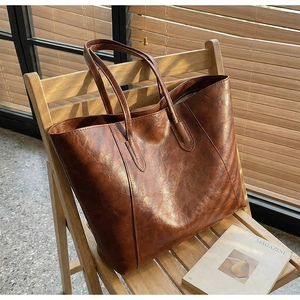 Close-up of vintage brown oil wax leather tote bag on wooden chair under natural light