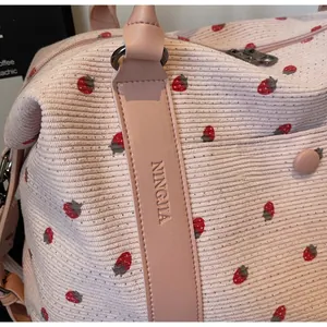 Close-up of pink corduroy fabric with strawberry print and embossed leather handle detail