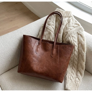 Close-up of vintage dark brown tote bag on white knit sweater in home setting